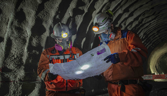Dos mineros revisando plano dentro de mina subterránea